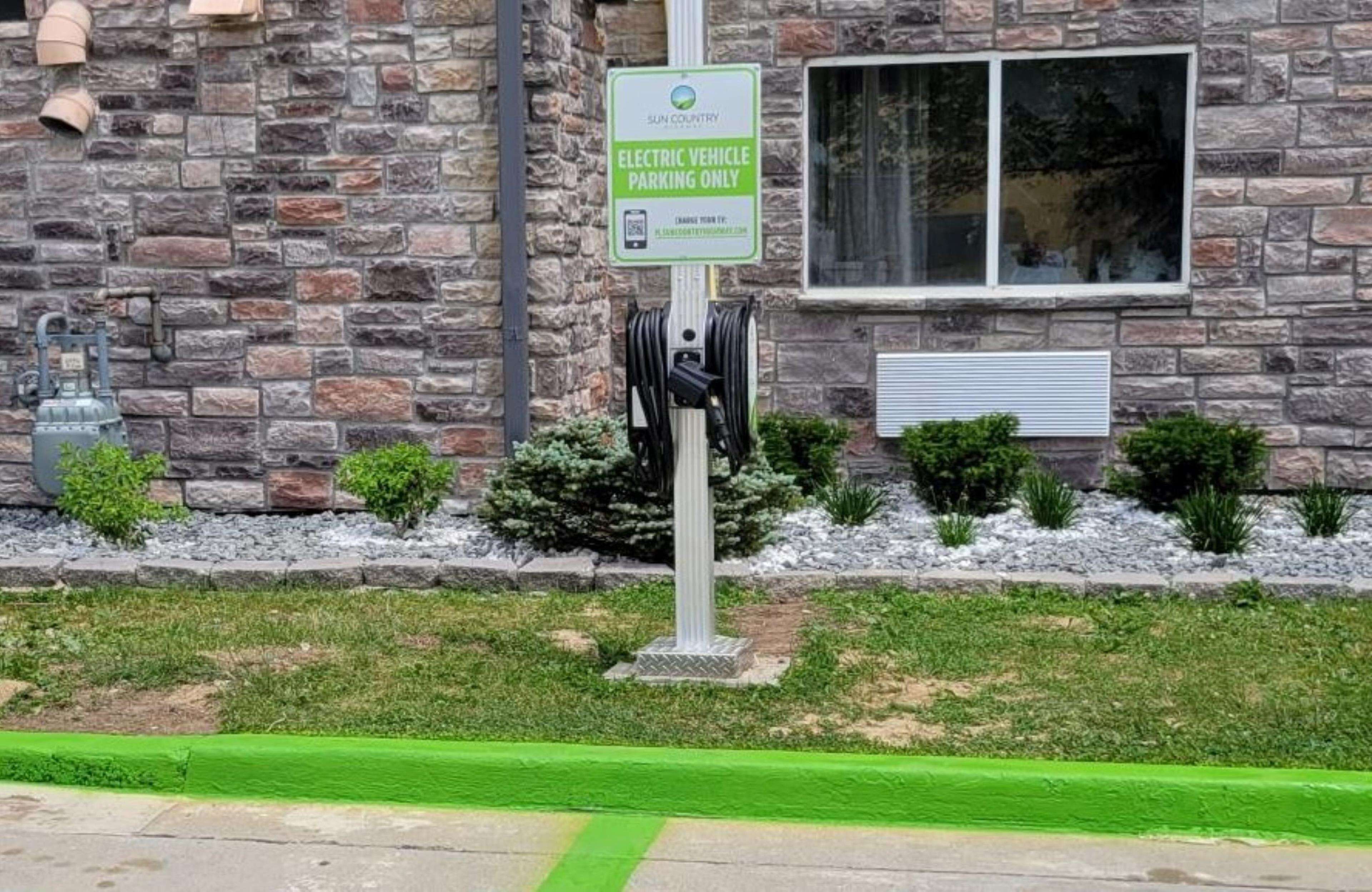 A sign indicating electric vehicle parking only, with a charging station attached.