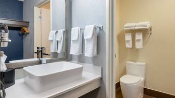 A modern bathroom with a large white sink, a mirror, and a toilet. There are multiple white towels hanging on a rack.