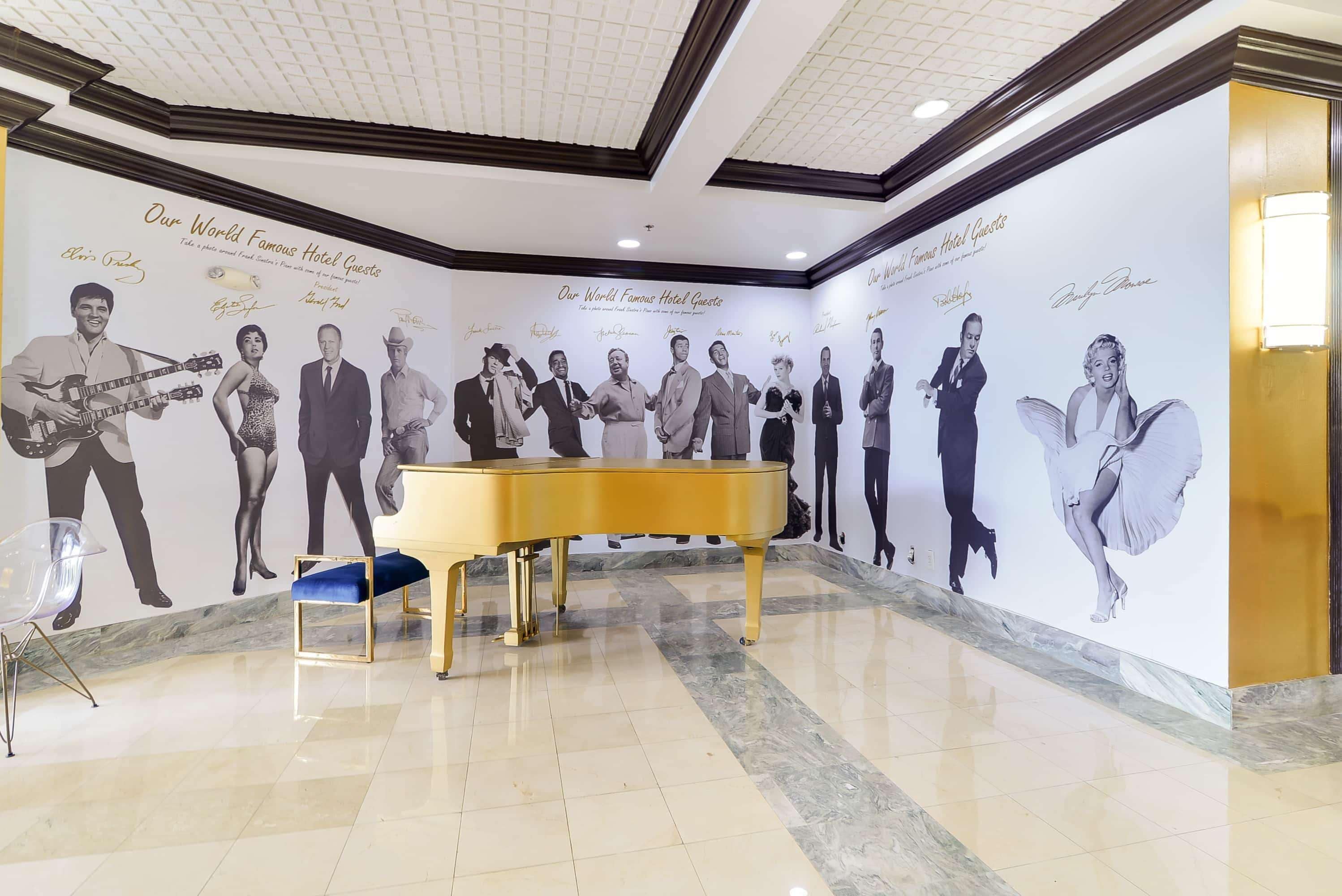 A lobby with a grand piano, a clear chair, and a wall featuring famous guests' portraits.