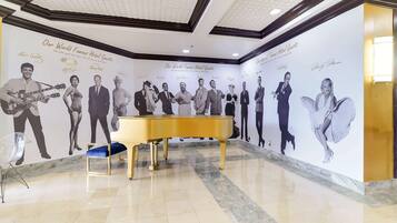 A lobby with a grand piano, a clear chair, and a wall featuring famous guests' portraits.