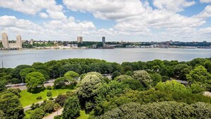 A cityscape with a large body of water, dense greenery, and various buildings including a prominent tower. - Riverside Tower Hotel (New York)