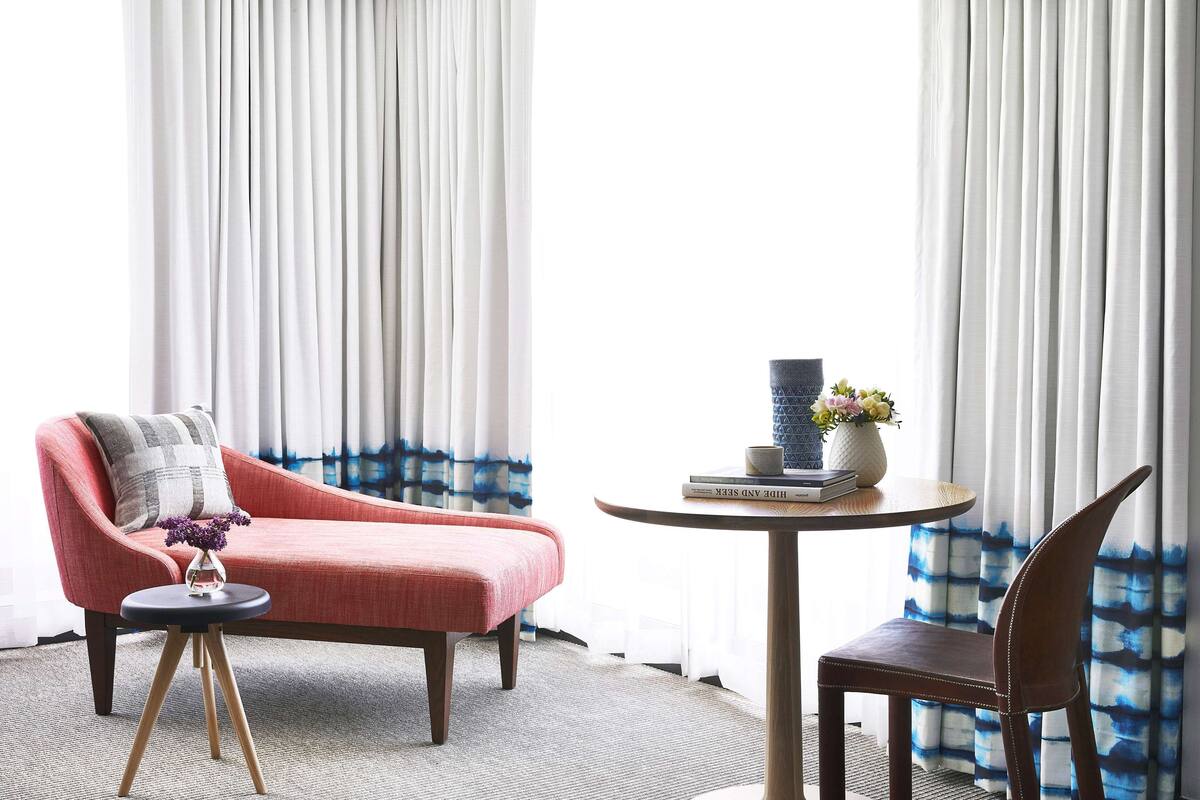 Ein Zimmer mit einem roten Sofa, einem runden Tisch mit einer Vase und Büchern sowie einem Sessel.