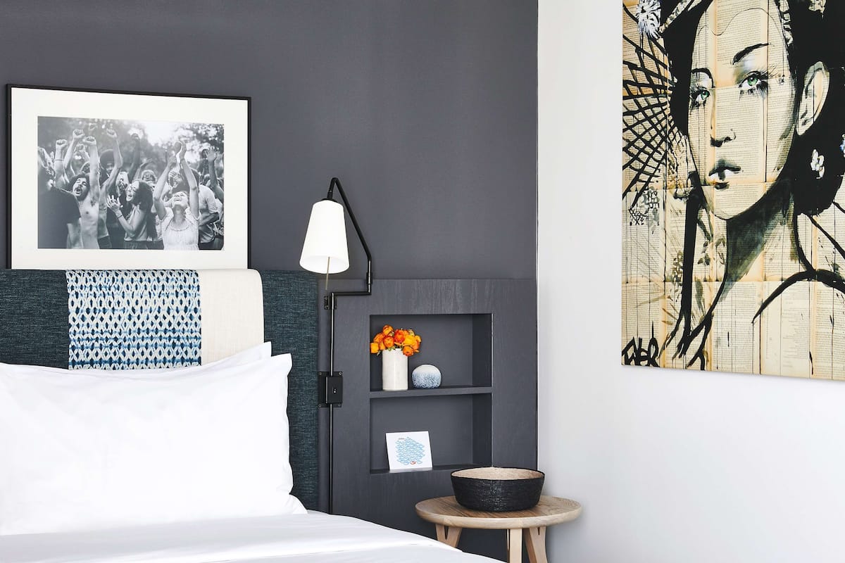Ein modernes Schlafzimmer mit einem Bett, einem schwarz-weißen Foto im Rahmen, einer Wandablage mit Blumen und einem großen abstrakten Gemälde.