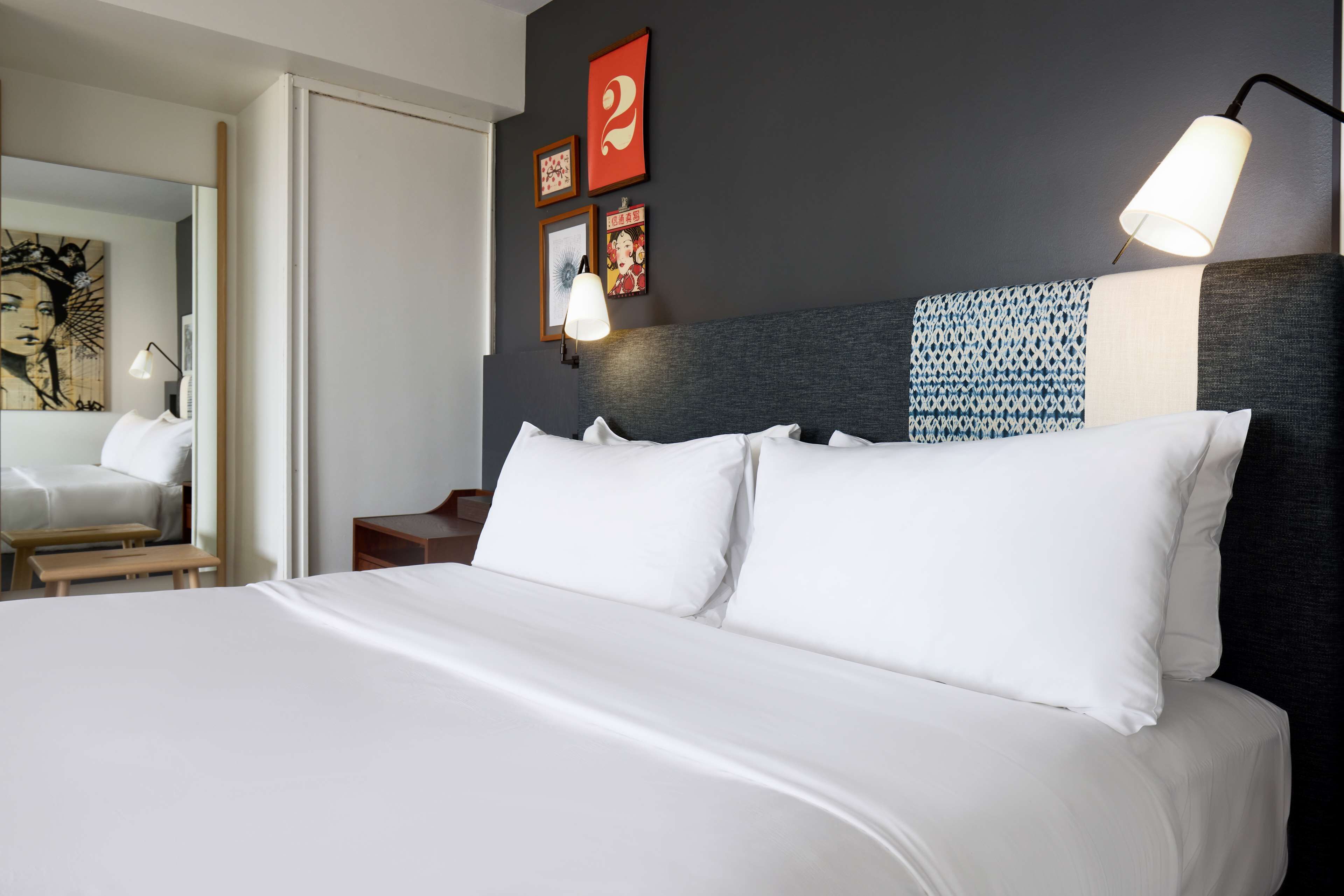 A neatly made bed with white linens, a headboard with a patterned design, and a bedside lamp.