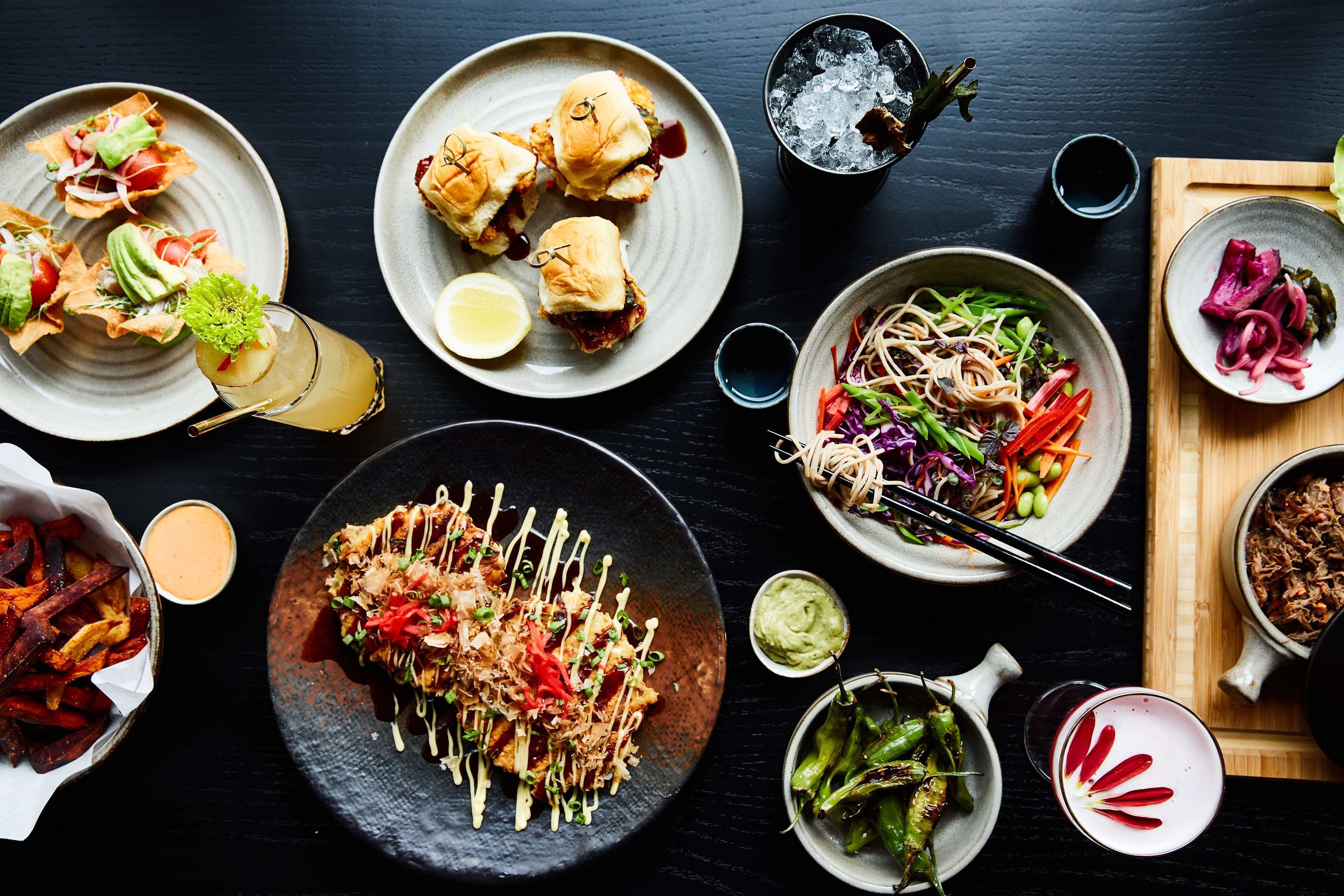 Eine Auswahl an Gerichten, darunter Sushi, Burger und Salate, präsentiert auf einem dunklen Tisch.