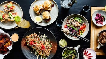 A variety of dishes including sushi, burgers, and salads, arranged on a dark table.