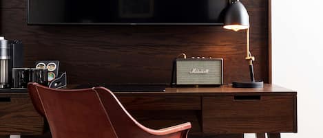 Una habitación de hotel moderna con una televisión de pantalla plana grande montada en una pared de madera, un escritorio con una silla de cuero, un amplificador Marshall y una cafetera.