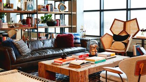 A modern living room with a leather sofa, a wooden coffee table with books, a bookshelf, and a large window. - Hotel Kabuki, part of JdV by Hyatt (San Francisco)