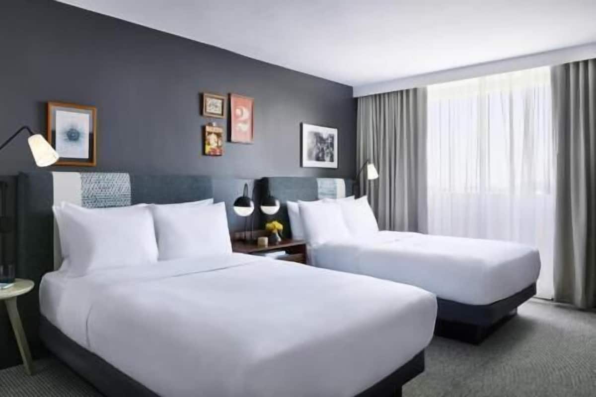 Ein Hotelzimmer mit zwei Betten, einem Schreibtisch, einer Lampe und einem Fenster mit Vorhängen.