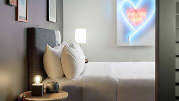 Habitación de hotel con cama, mesita de noche con lámpara, letrero de neón y cuadros en la pared.