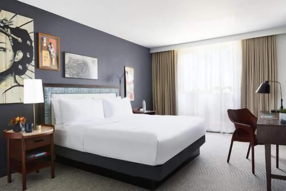 Ein Hotelzimmer mit einem großen Bett, einem Schreibtisch, einem Sessel und Bildern an den Wänden.
