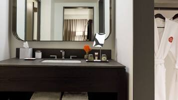A modern bathroom with a large mirror, a sink, a towel rack, and a robe hanging on a hook.