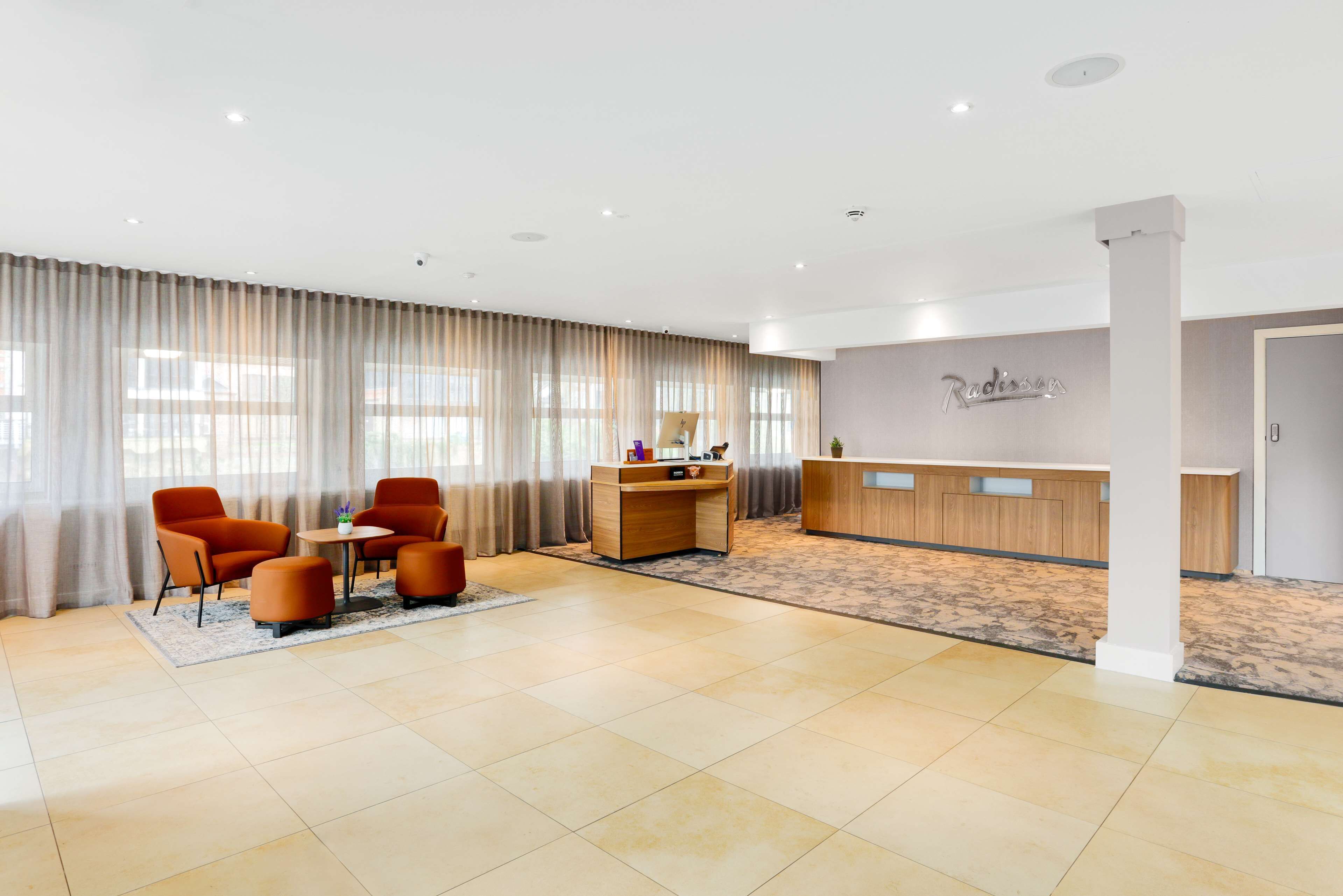 A spacious lobby with a reception desk, a seating area with chairs, and a large window with curtains.
