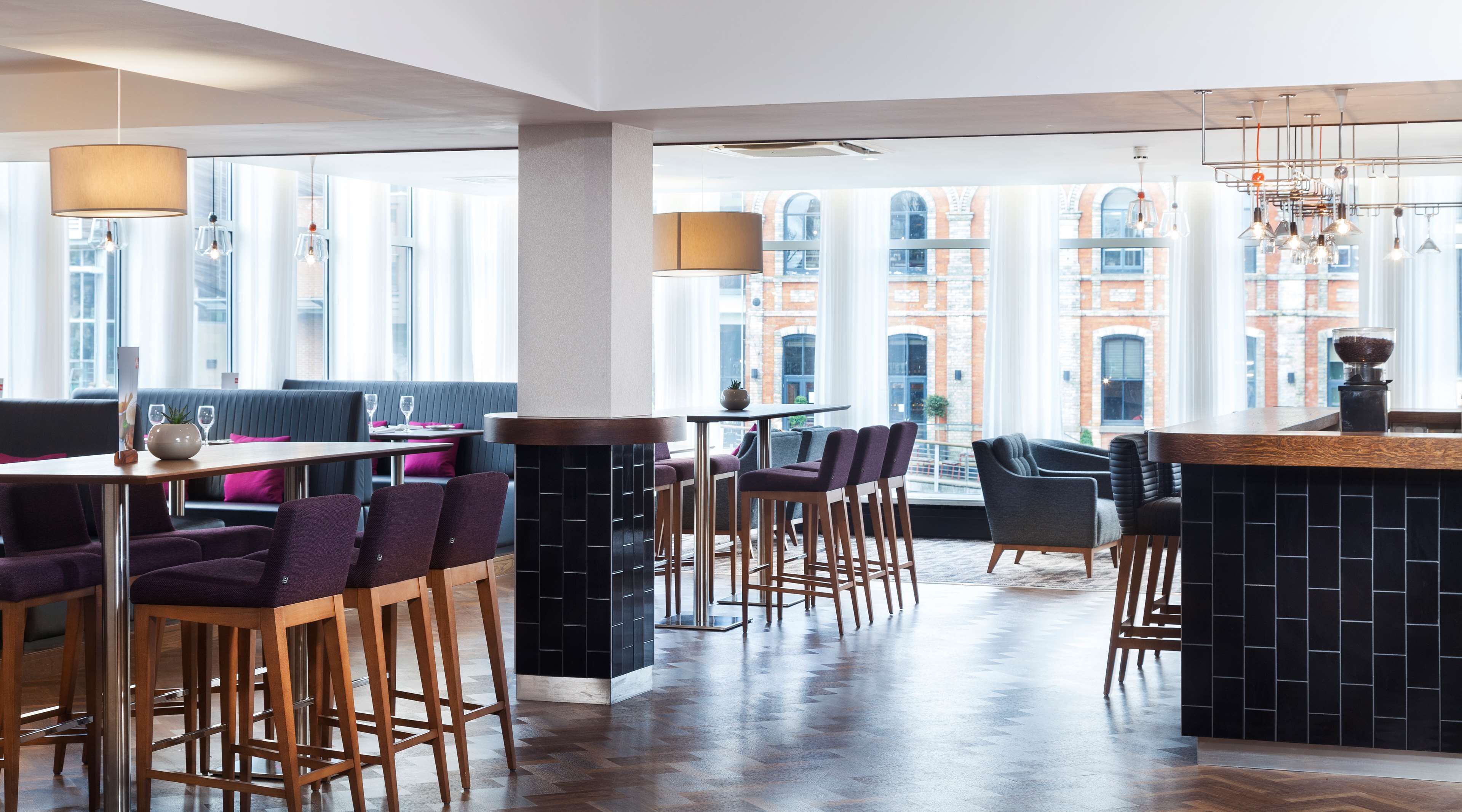 A modern restaurant with high ceilings, large windows, and a mix of seating options including bar stools and booths.