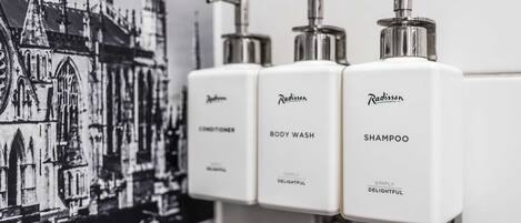 A bathroom with three white dispensers labeled Radisson Conditioner, Body Wash, and Shampoo.