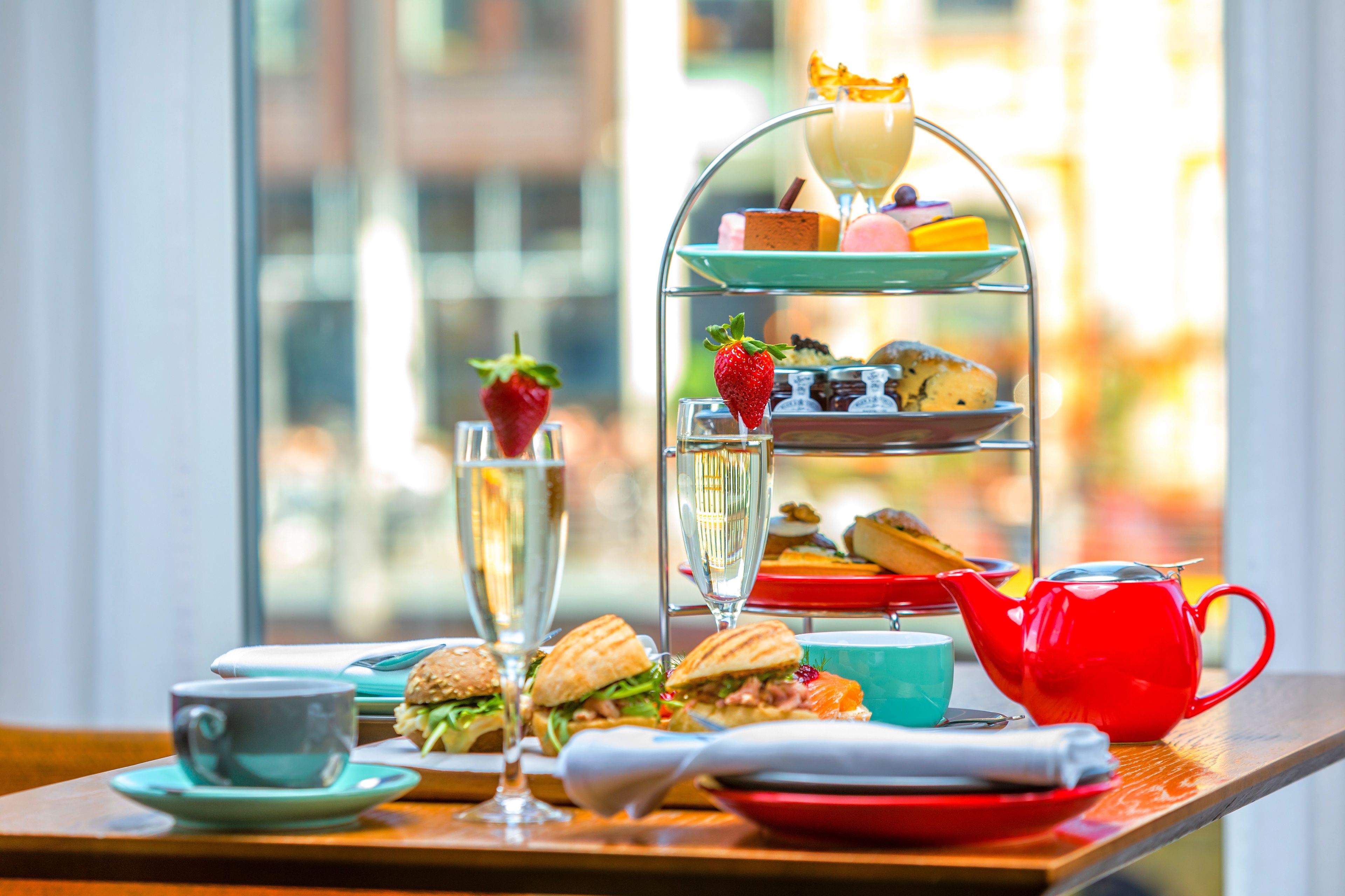 A tiered dessert stand with various pastries and a red teapot on a table.