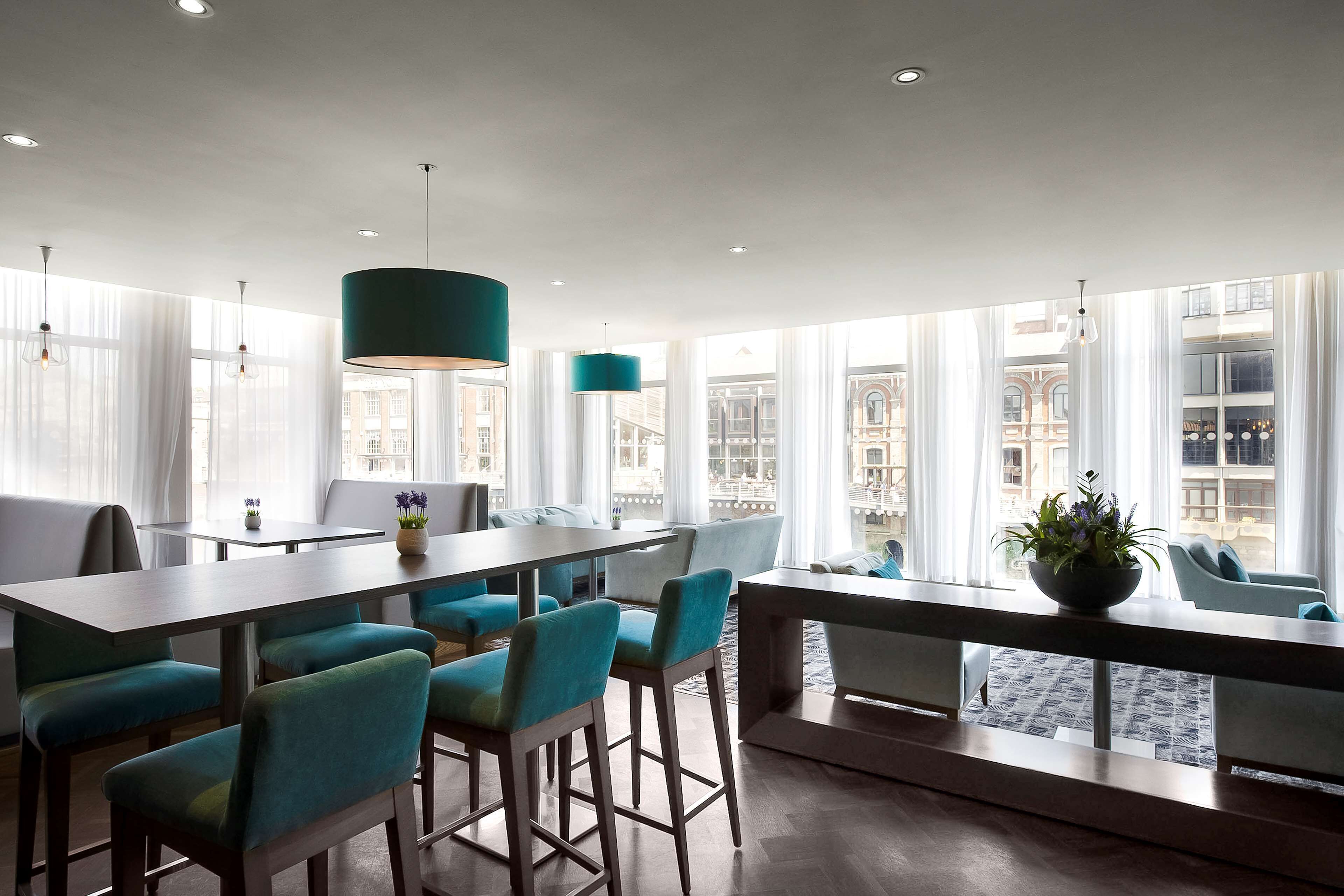 Una habitación de hotel moderna con zona de comedor, ventanas amplias y vista a la ciudad.