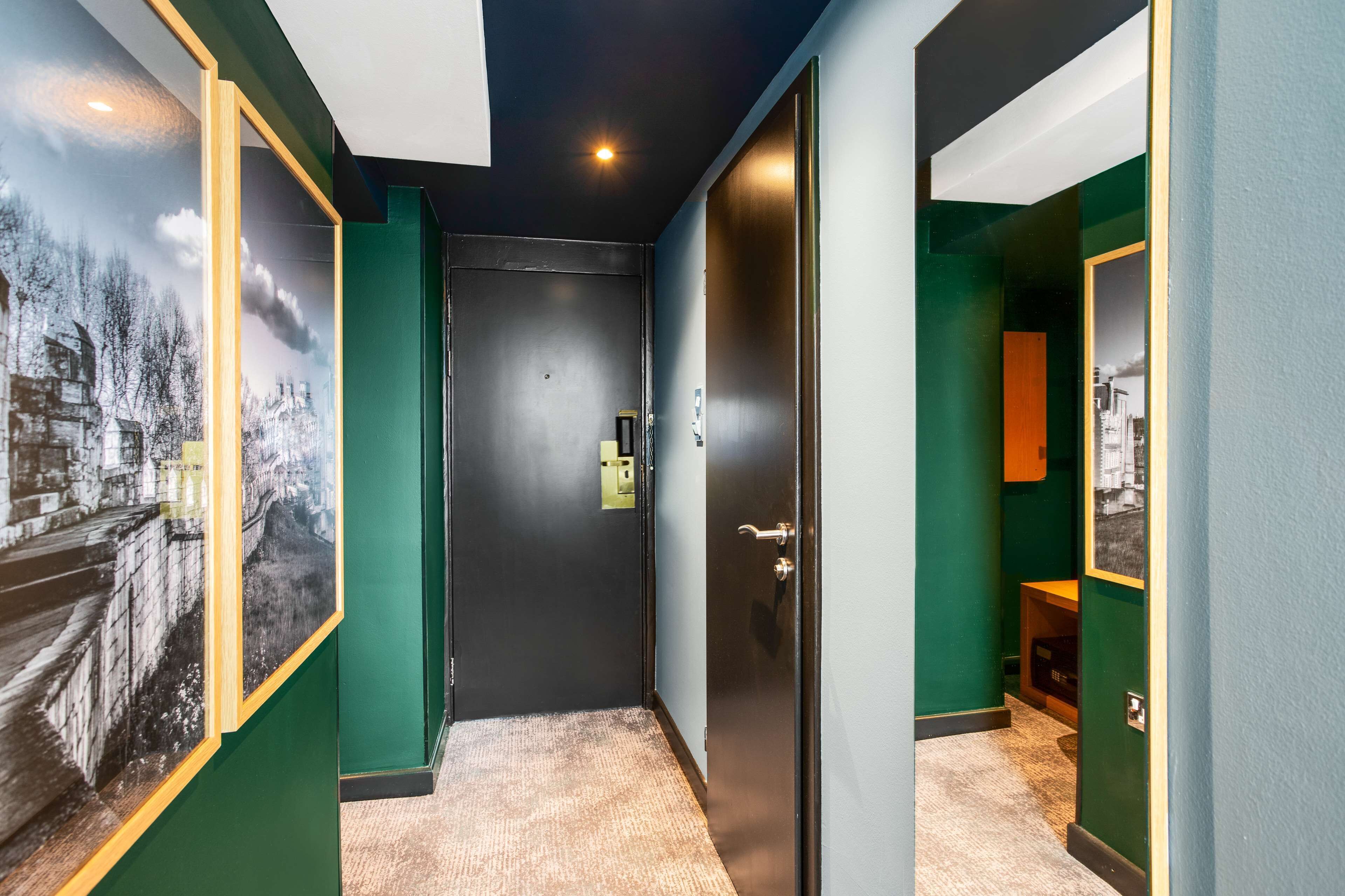 A hallway with green walls, a black door, and a framed picture on the left.