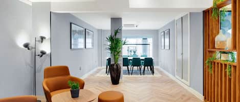 Un interior moderno con suelo de madera en espiga, una planta central, asientos naranjas y una zona de comedor con sillas verdes.