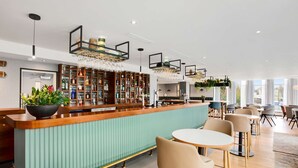 Un espace bar moderne avec un comptoir vert, des étagères en bois où sont exposées des bouteilles, et divers types de sièges, notamment des tables et des chaises rondes.