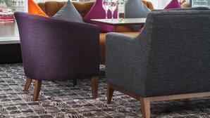 Une chambre d’hôtel moderne avec de grandes fenêtres, une vue sur la ville, un canapé et une table avec une bouteille de vin.
