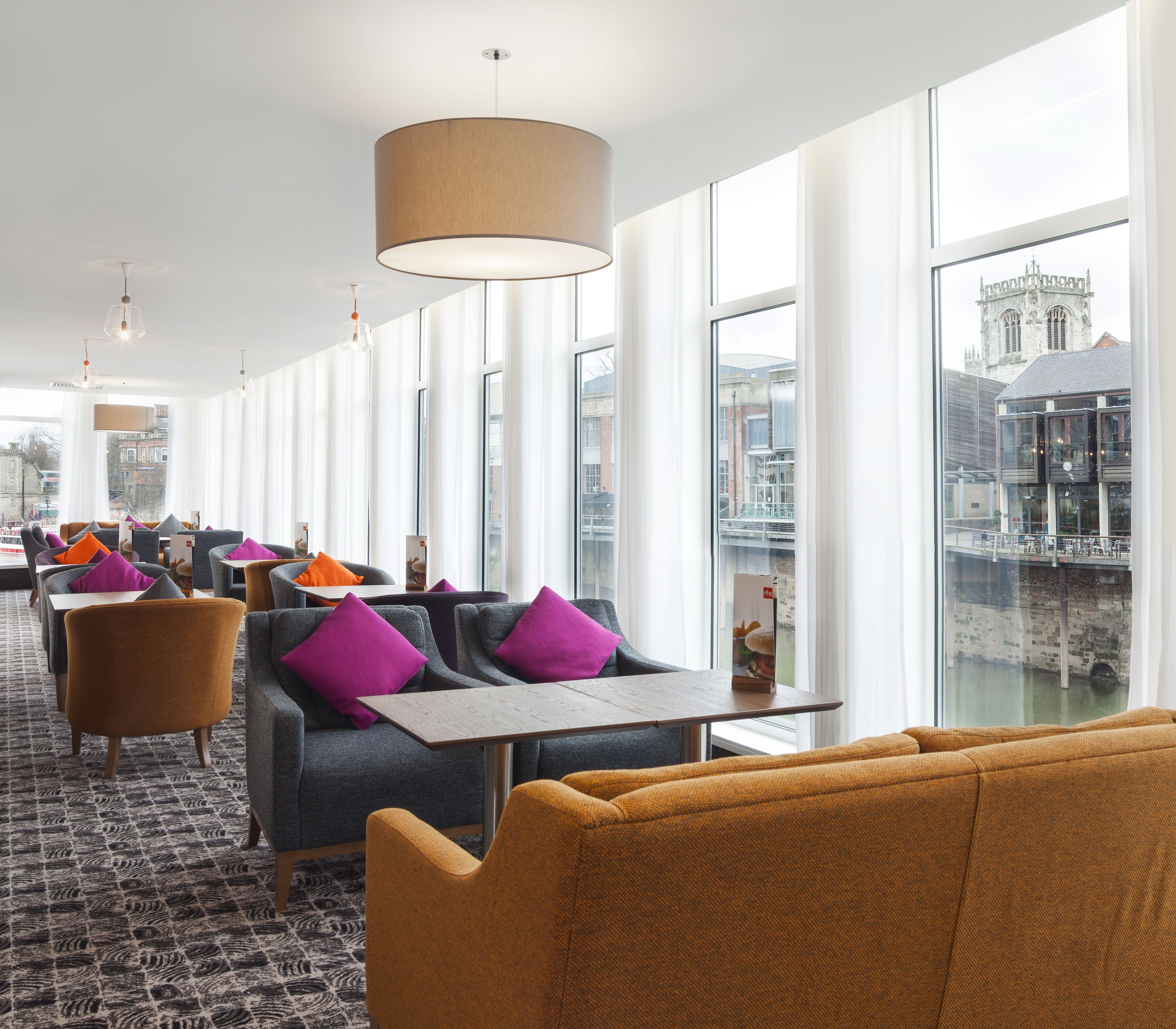 A modern hotel lobby with seating areas, large windows, and a view of a historic building.