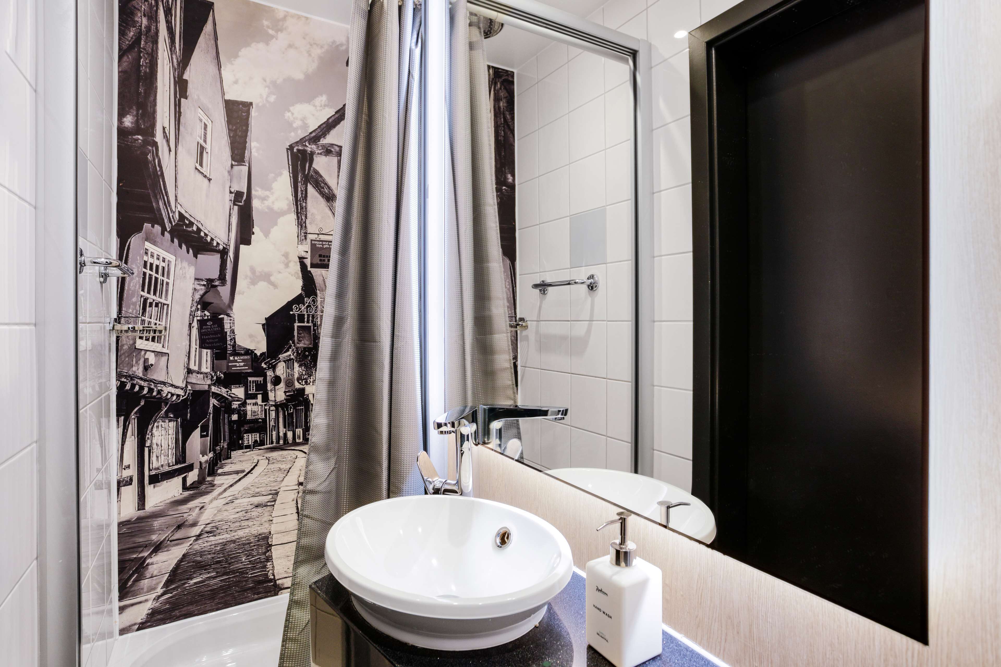 A modern bathroom with a large mirror, a white sink, and a shower curtain.