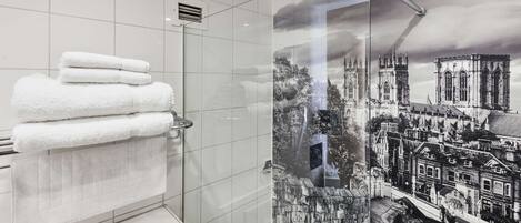 A modern bathroom with a glass shower enclosure, a stack of white towels, and a cityscape mural on the wall.