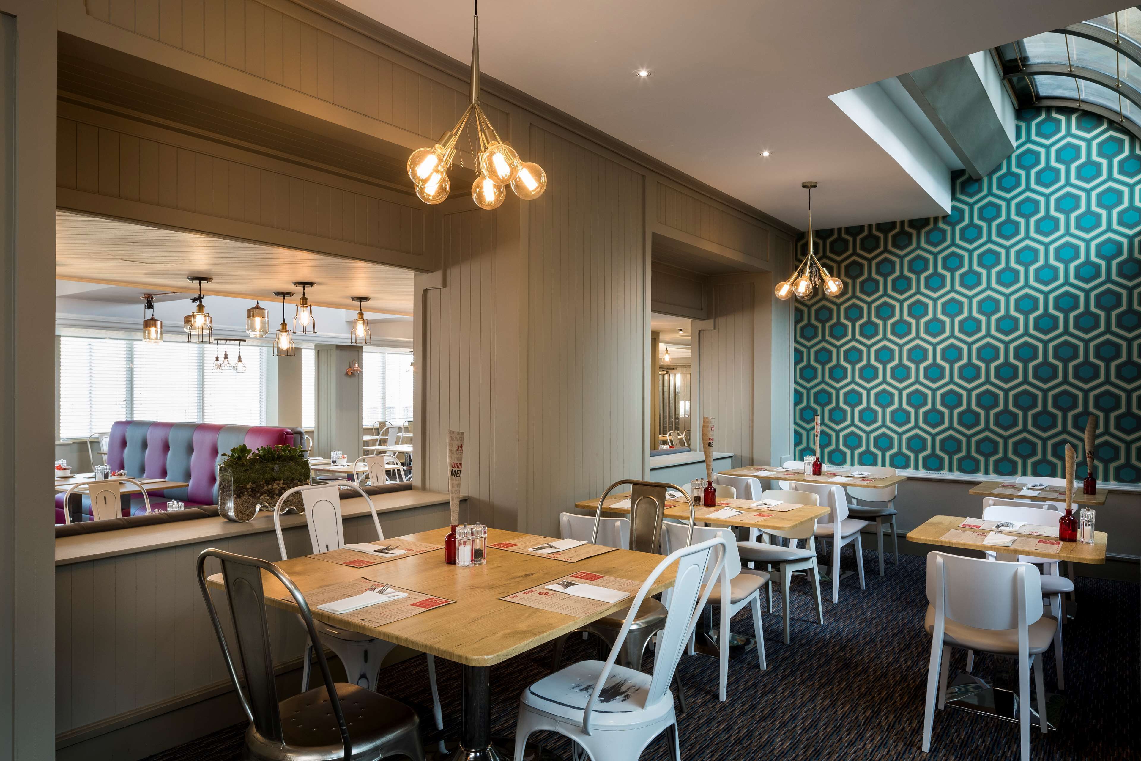 A restaurant with wooden tables, white chairs, and pendant lighting.