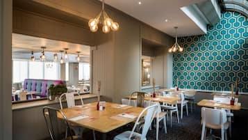 A restaurant with wooden tables, white chairs, and pendant lighting.