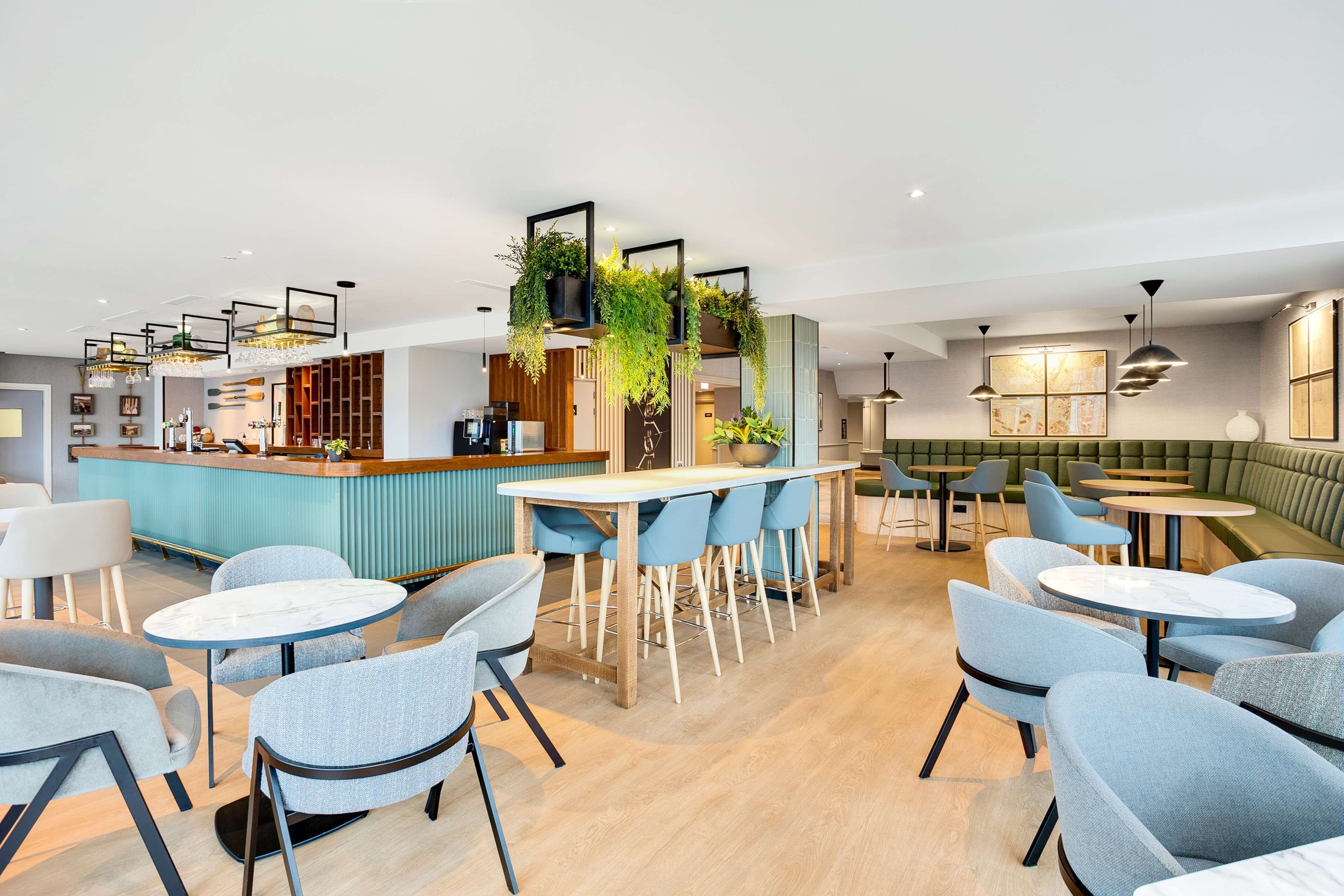 A modern restaurant with a bar area, seating arrangements, and decorative plants.