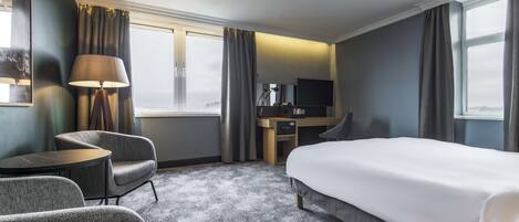 Una habitación de hotel con cama, escritorio, silla, lámpara y televisión.