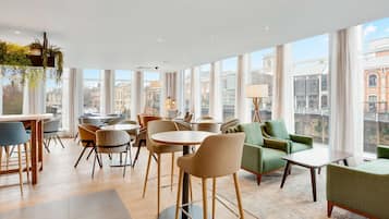 Un moderno vestíbulo de hotel con ventanas amplias, una zona de comedor y asientos cómodos.