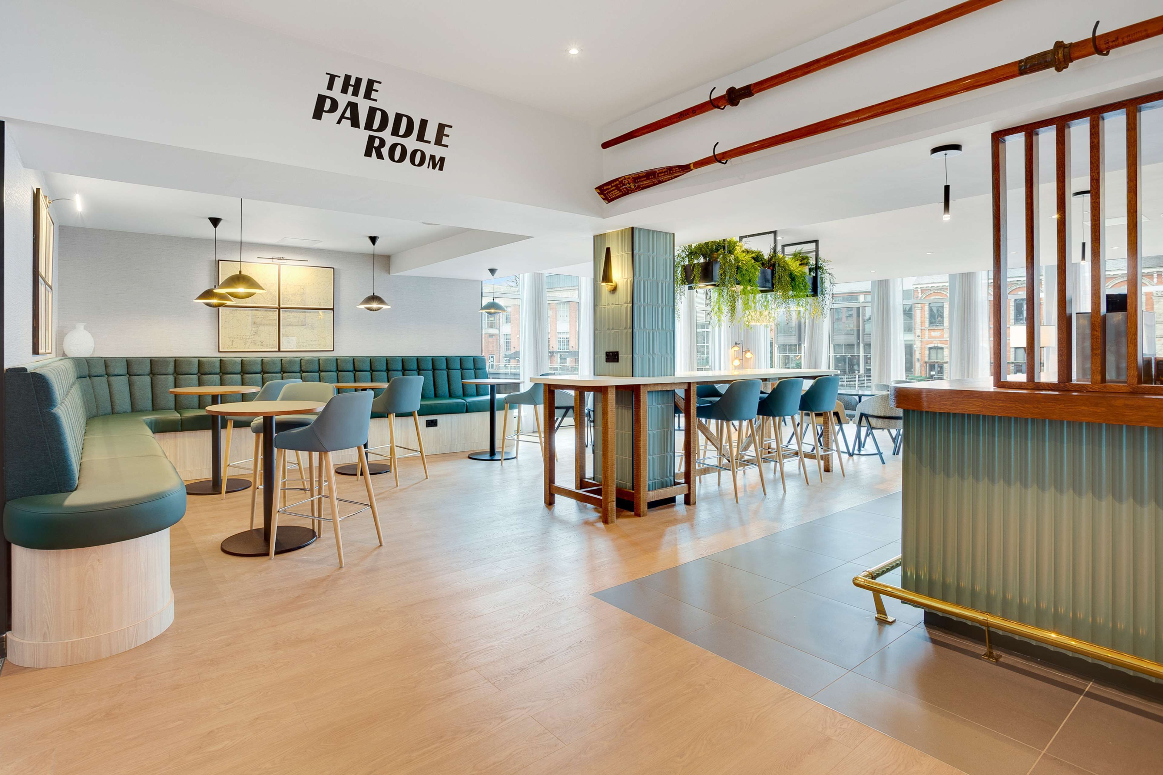 A modern room with a green sofa, wooden tables, and chairs. There is a sign that reads "THE PADDLE ROOM".