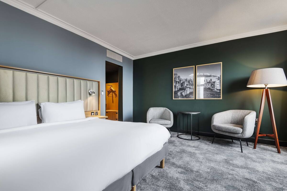 A hotel room with a large bed, two armchairs, a small table, and a floor lamp.