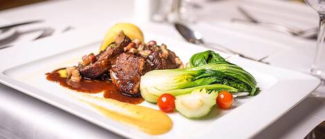 Un plato rectangular blanco con un bistec, verduras y salsa.