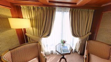 A room with two striped armchairs, a glass table with a vase, and curtains.