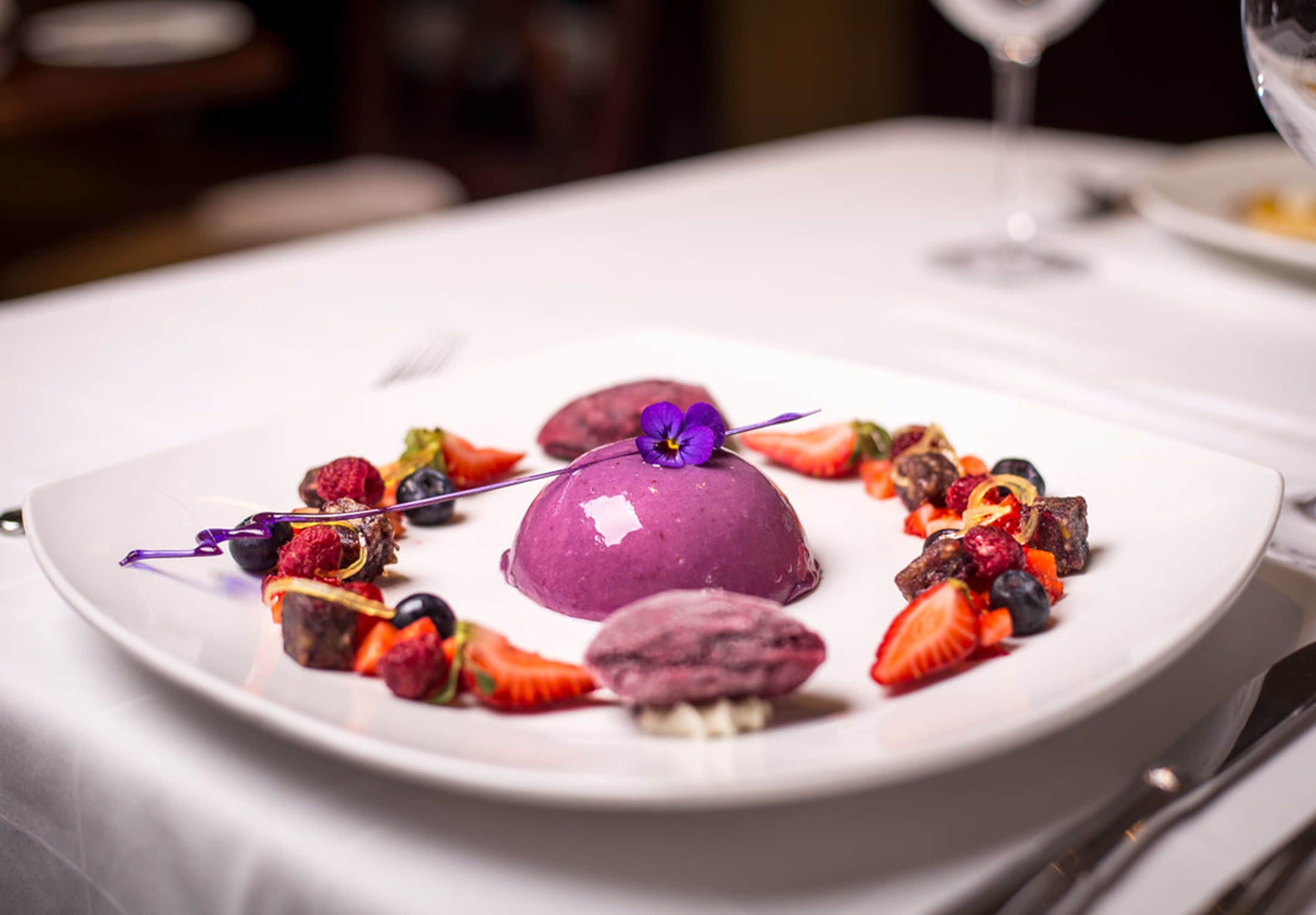 A dessert plate with various fruits and a purple dessert centerpiece.