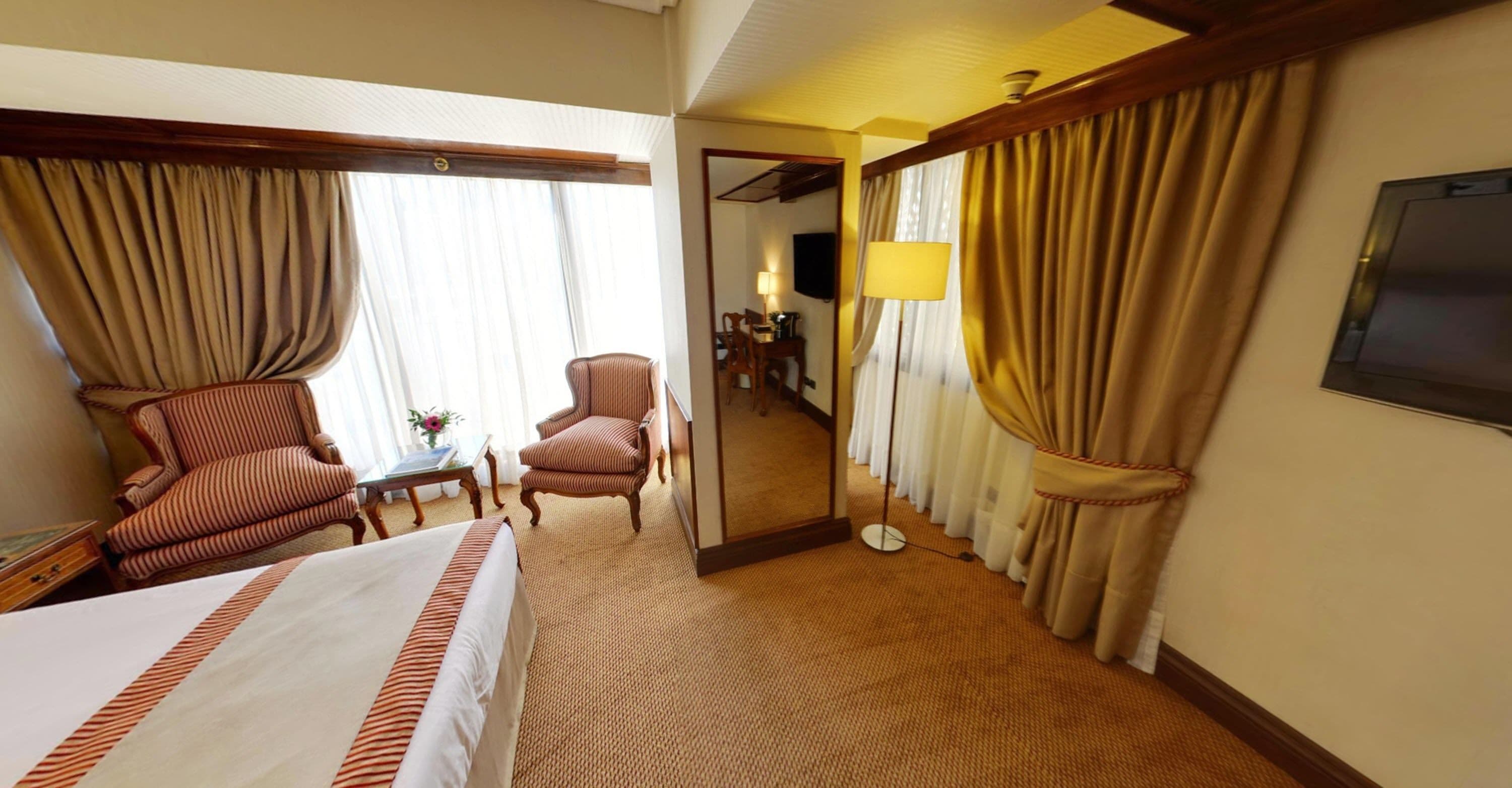 Une chambre d’hôtel avec un lit, deux fauteuils à rayures, une petite table, une lampe et un téléviseur.