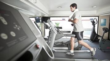 A man running on a treadmill in a gym with exercise equipment and a window with a view.