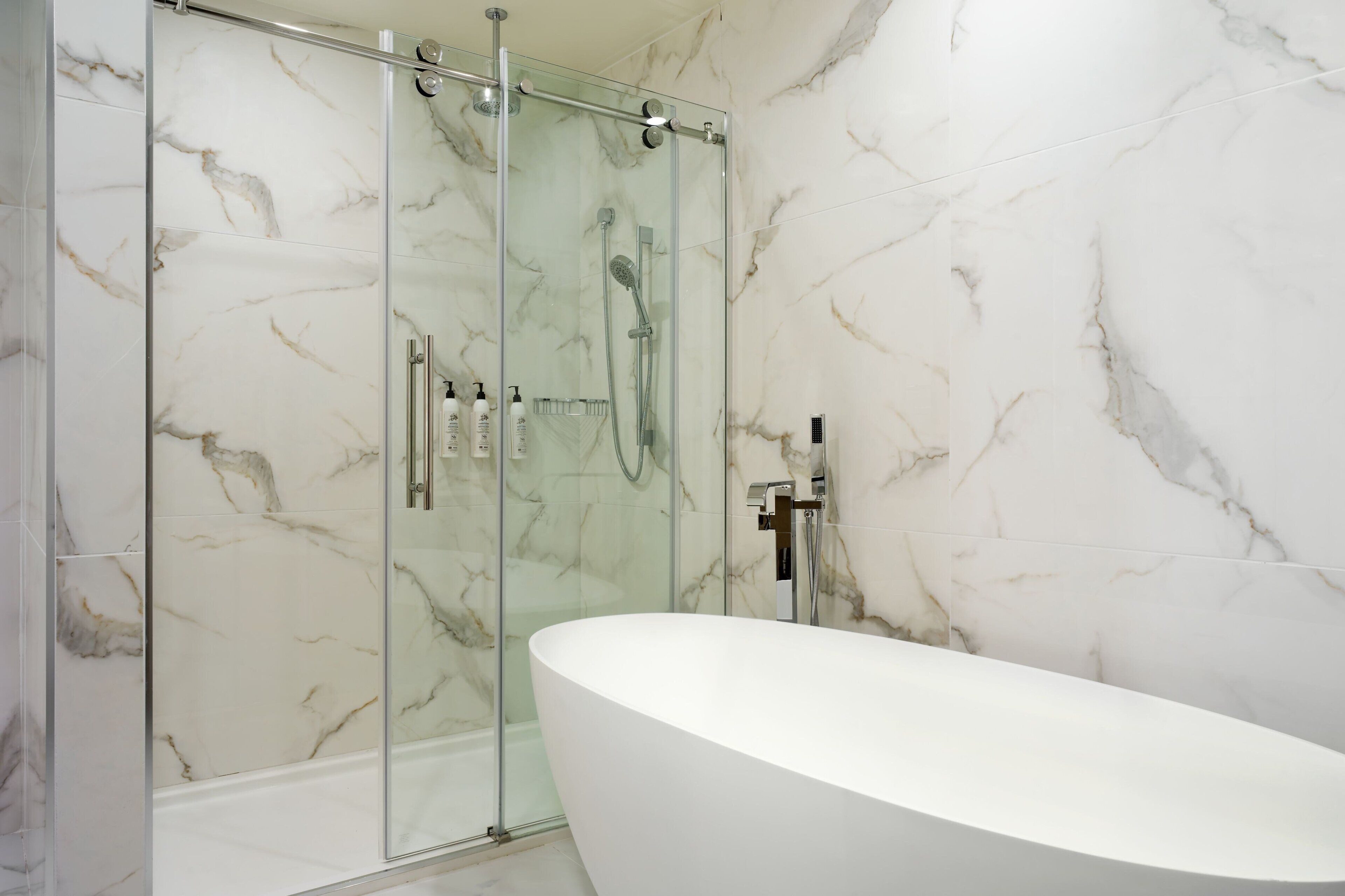 A modern bathroom with a glass-enclosed shower, a freestanding bathtub, and marble walls.
