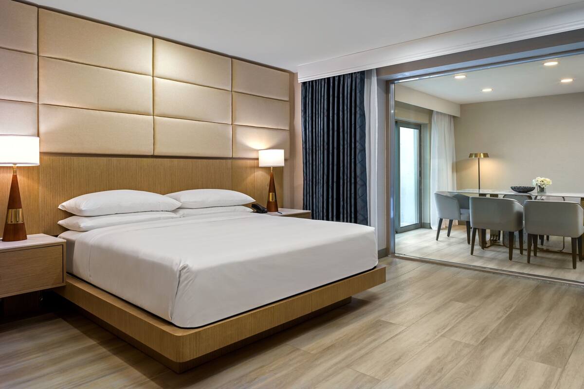 A modern hotel room with a large bed, bedside tables, a desk, and chairs.