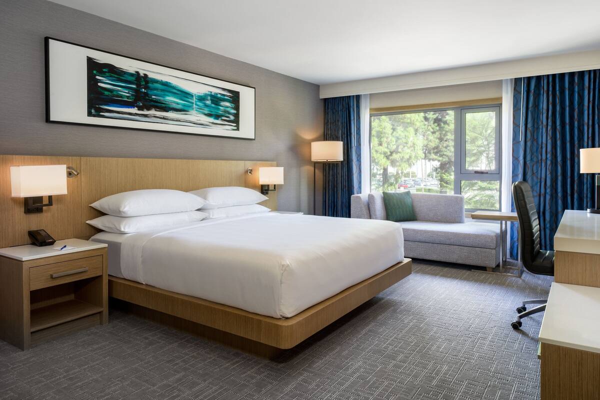A hotel room with a large bed, bedside tables, a desk, and a window with curtains.