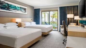 Habitación de hotel con dos camas, un escritorio, una silla, un televisor y un ventanal con cortinas.