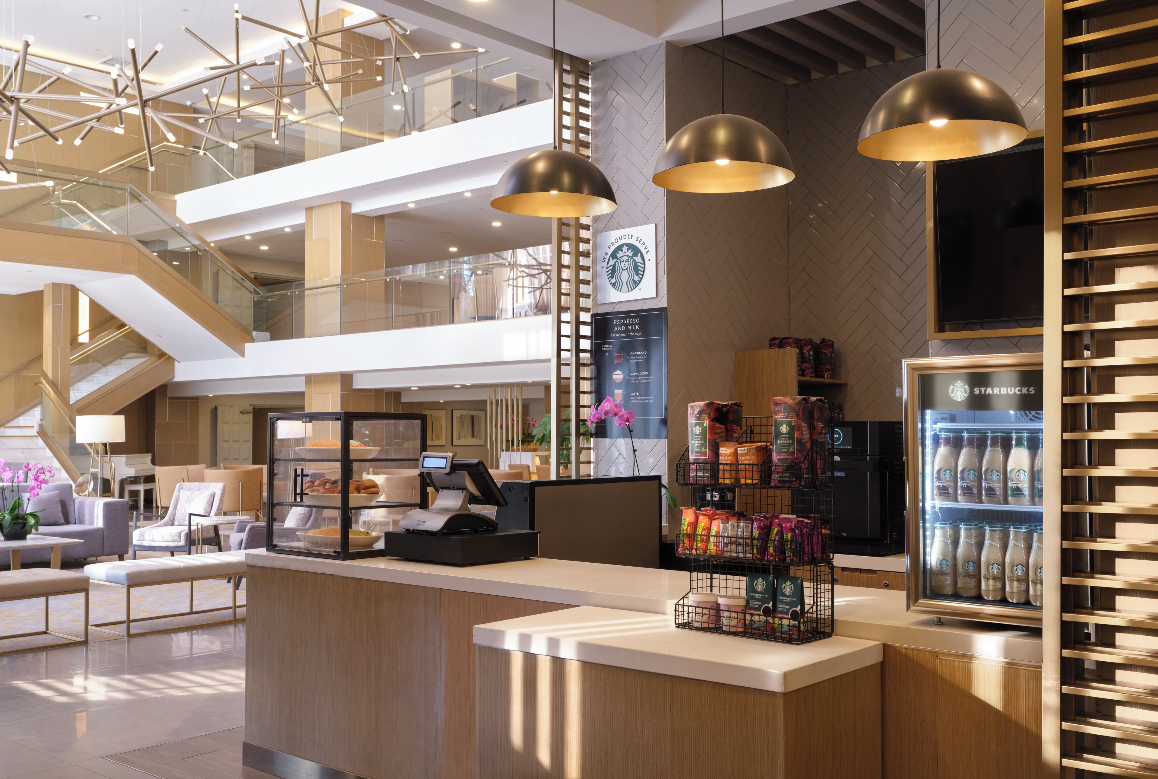 Un moderno vestíbulo de hotel con un mostrador de recepción, una máquina de café y una presentación de Starbucks.