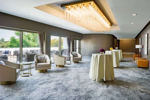 A spacious room with a large window, a chandelier, and a carpeted floor.