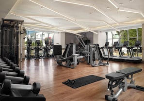 Un gimnasio moderno con diversos equipos de ejercicio, ventanas amplias y piso de madera.