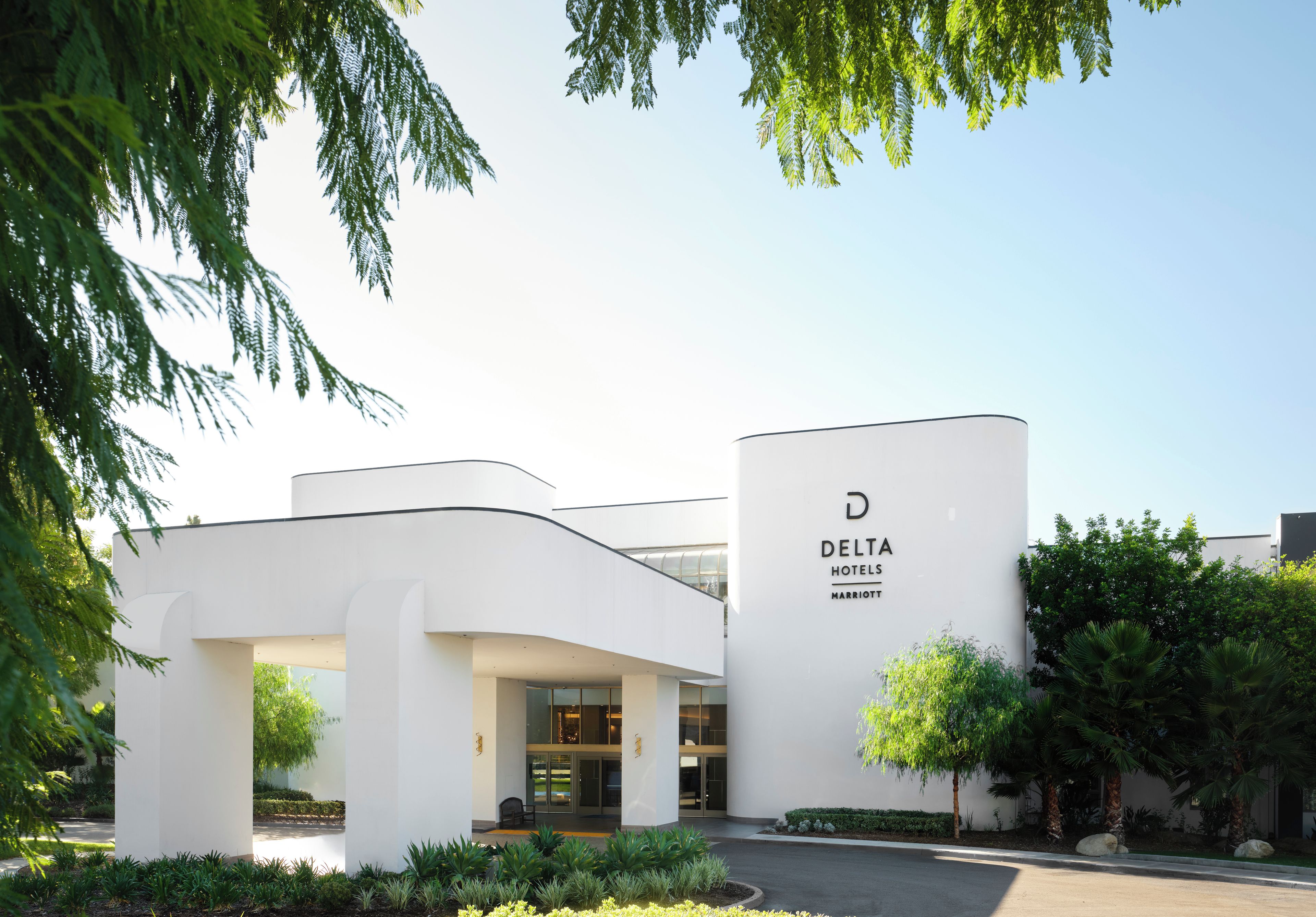 Entrada moderna de un hotel con cielo despejado, un cartel de Delta Hotels Marriott y un jardín bien cuidado.