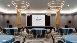 A conference room with multiple round tables, chairs, and a stage with a screen displaying the Delta Hotels logo. - Delta Hotels by Marriott Ontario Airport (Ontario)