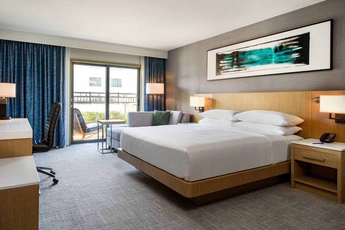 A hotel room with a large bed, a desk, a chair, and a view of the outdoors.